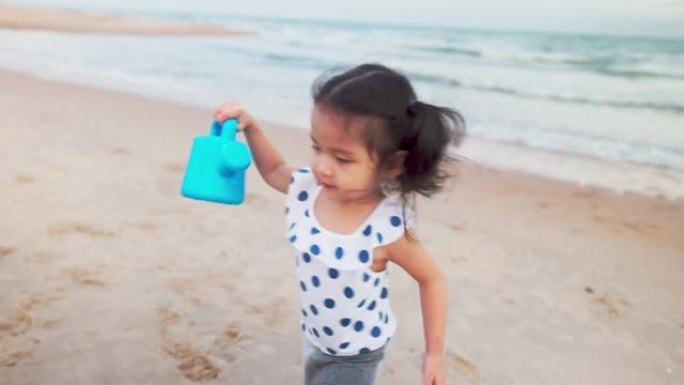 可爱的蹒跚学步的孩子在沙滩上倒水。