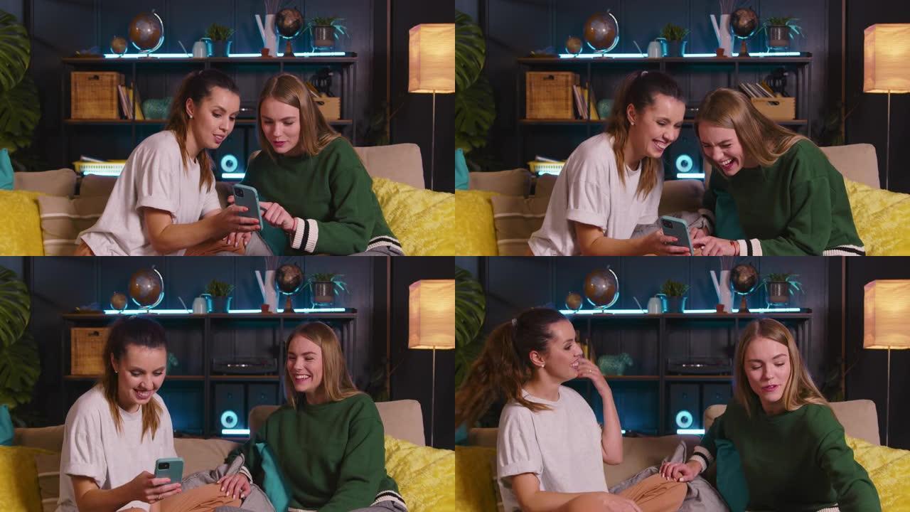 两个快乐的年轻美丽的高加索女性朋友在智能手机上观看有趣的视频，在舒适的家中在沙发上大笑。