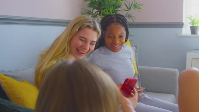 一群多元文化的少女朋友看着坐在沙发上的手机在家里的卧室里闲逛-慢动作拍摄