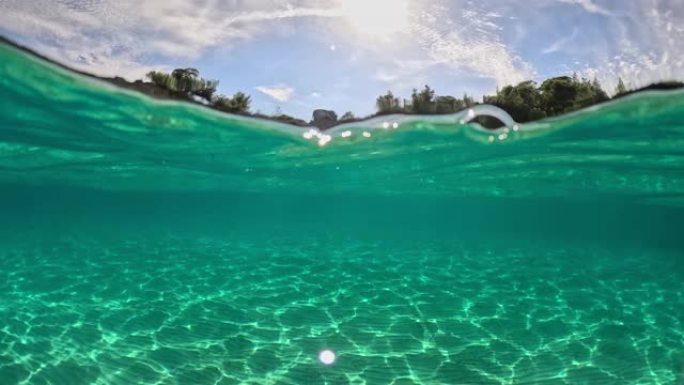 半水下慢动作拍摄热带海滩，海水清澈见底。从海里看。沙滩、岩石、树木和水面