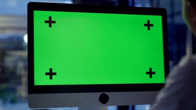 深夜办公室里有绿色chromakey复制空间的电脑屏幕。业务人员正在查看带有跟踪标记的监视器，以在线