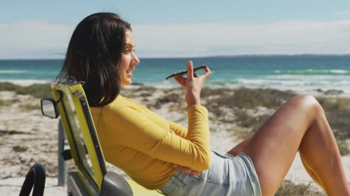 白人妇女躺在海边的越野车上，在智能手机上聊天