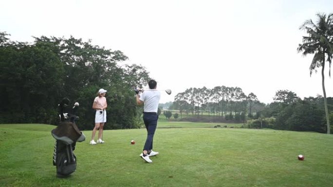 慢动作亚洲中国男高尔夫球手与妻子在高尔夫球场上开球