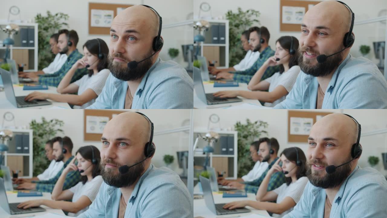 戴着耳机的有吸引力的家伙与办公室技术客户支持部门的客户交谈