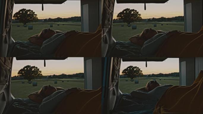 DS女人躺在黄昏时停在草地上的露营车的小屋里