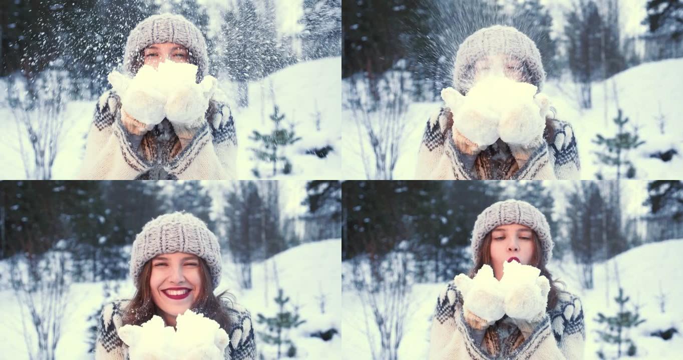 冬天的心情。特写美丽的年轻幸福的女人戴着帽子，手套在森林慢动作的镜头前吹雪