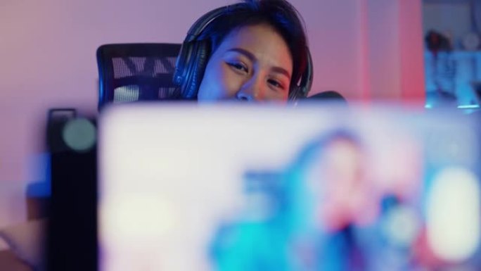 快乐亚洲女孩博主音乐影响者使用智能手机广播录音佩戴耳机在线直播晚上在客厅家庭工作室与听众交谈。
