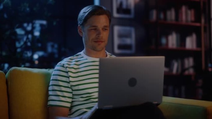 男人在家庭办公室使用笔记本电脑，晚上做远程工作。坐在沙发上的英俊男性在电脑上工作，头脑风暴创意项目，