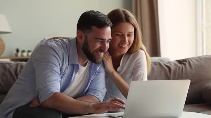 微笑的年轻家庭夫妇在笔记本电脑屏幕前在沙发上放松