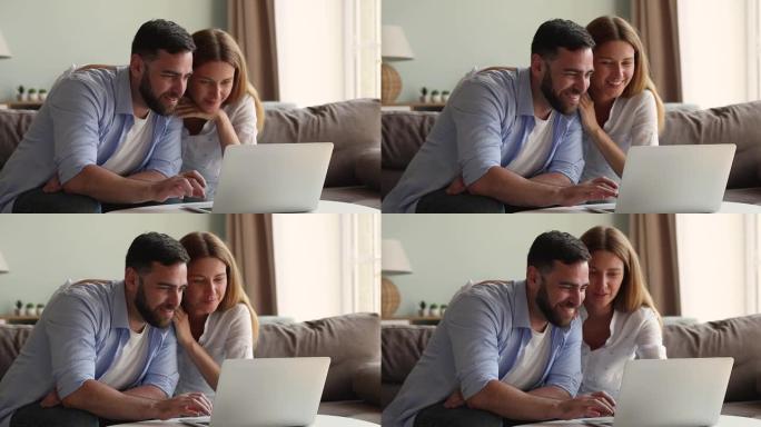微笑的年轻家庭夫妇在笔记本电脑屏幕前在沙发上放松