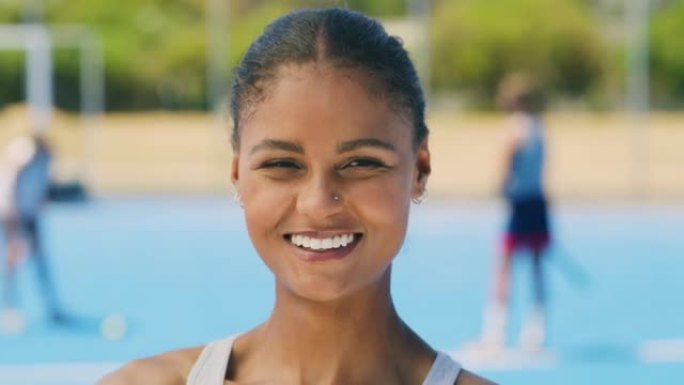 快乐的年轻混血青少年曲棍球运动员站在运动场上的肖像。面对充满自信的微笑的高中运动员，有动力并准备与她
