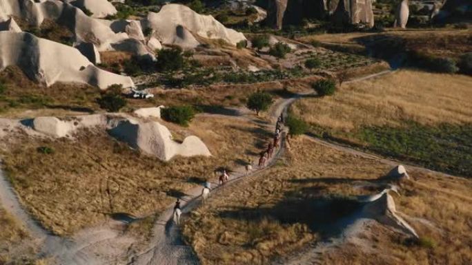 美丽宽阔的空中背景，一列骑马者在夏季卡帕多西亚之旅中沿着阳光明媚的岩石缓慢移动。