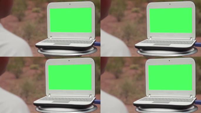 男子在户外凳子上使用带绿屏的笔记本电脑。放大。4K。