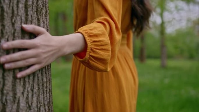 追踪，无法辨认的橙色连衣裙女性的特写镜头，以慢动作将她的手放在树皮上