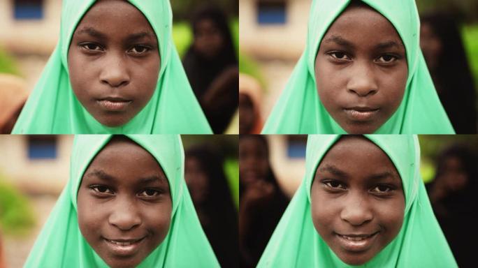 一个害羞的真实非洲女孩在镜头前微笑的特写肖像，背景中模糊的孩子在玩耍。黑人女性儿童对世界的未来和团结