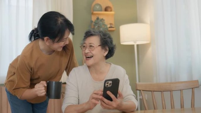年轻的亚洲女性正在冷静地教她的母亲如何使用智能手机。