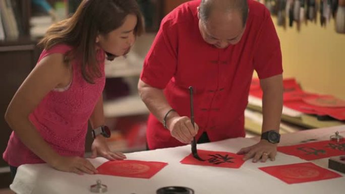 一位亚洲中国男性为即将到来的农历新年庆祝活动而练习中文中文，目的是繁荣和良好的措辞，方法是将其写在红