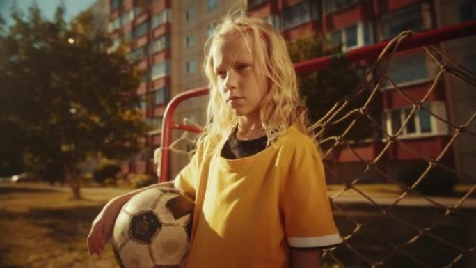 一个穿着黄色t恤的专注女孩在附近的田野里拿着足球的肖像。年轻的女子足球运动员看着镜头。运动、童年、友