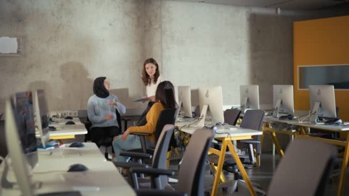 不同的多种族女学生坐在信息图表室里，合作进行一个大学项目。年轻学者谈，研究软件开发或计算机科学。