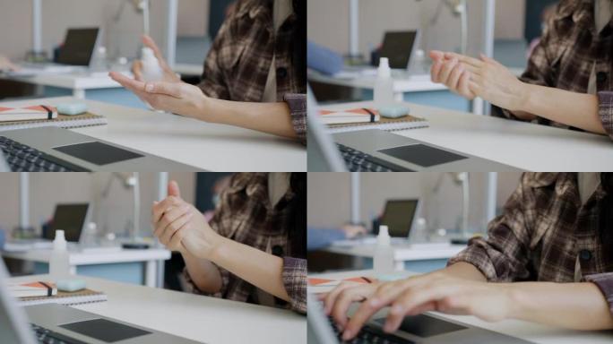 女人用消毒剂清洁手，然后在办公室用笔记本电脑工作的特写镜头