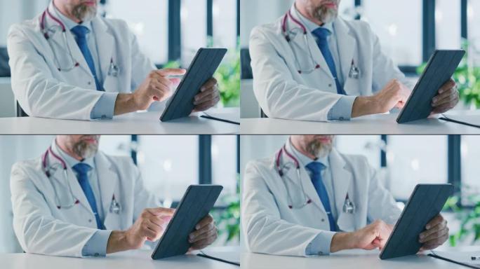 在健康诊所的平板电脑上工作的家庭医生的特写镜头。穿着白大褂的医生正在医院办公室的桌子后面浏览病史。