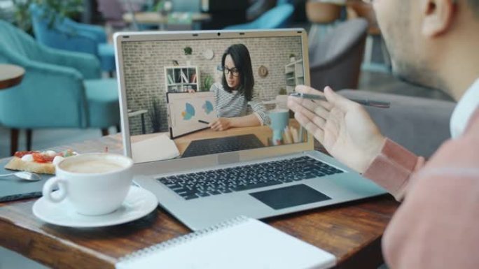 阿拉伯男子在视频通话中与女性伴侣交谈，看着咖啡馆餐桌上的笔记本电脑屏幕
