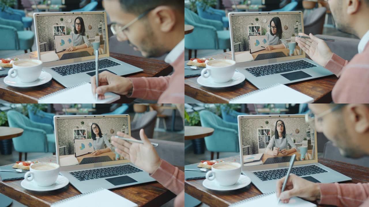 阿拉伯男子在视频通话中与女性伴侣交谈，看着咖啡馆餐桌上的笔记本电脑屏幕
