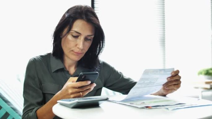 女人检查他的银行对帐单并使用智能手机，在智能手机上在线支付账单