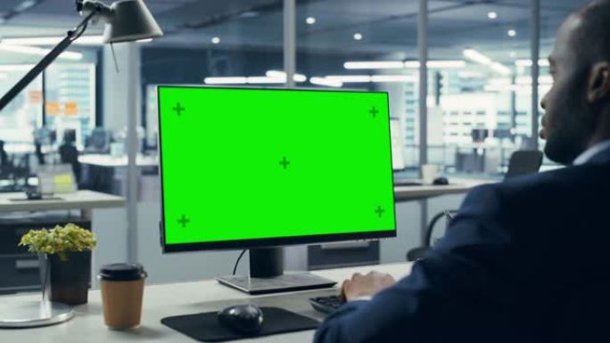成功的黑人商人坐在办公桌前，在办公室里用绿屏笔记本电脑工作。使用色度键显示的非裔美国商人。肩以上静态