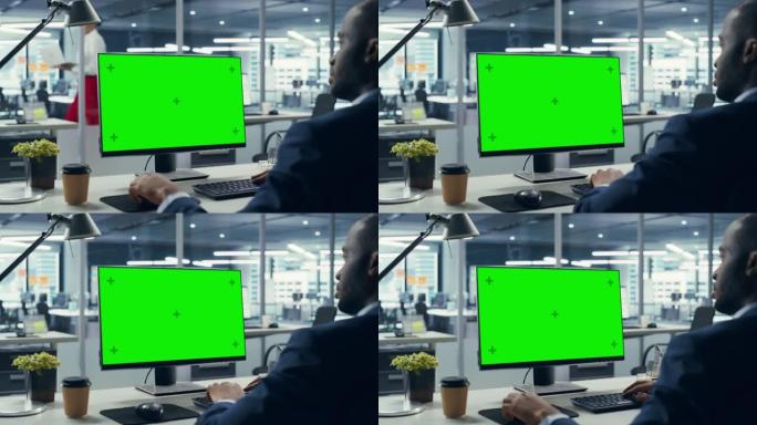 成功的黑人商人坐在办公桌前，在办公室里用绿屏笔记本电脑工作。使用色度键显示的非裔美国商人。肩以上静态