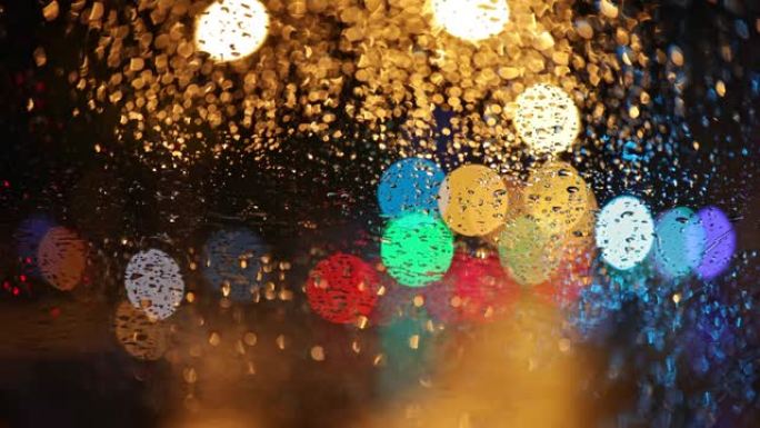 夜城的五彩灯和路过的汽车在雨滴中穿过汽车的玻璃。抽象博克秋雨城市背景