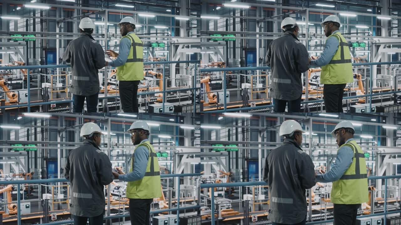 多种族经理和非裔美国人汽车工厂工程师穿着制服，使用平板电脑。汽车行业4.0制造员工讨论车辆装配厂的工