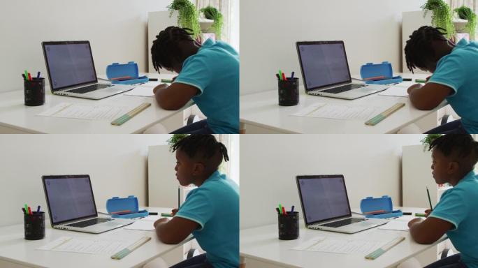 非裔美国男孩正在做作业，看着家里有复印空间的笔记本电脑