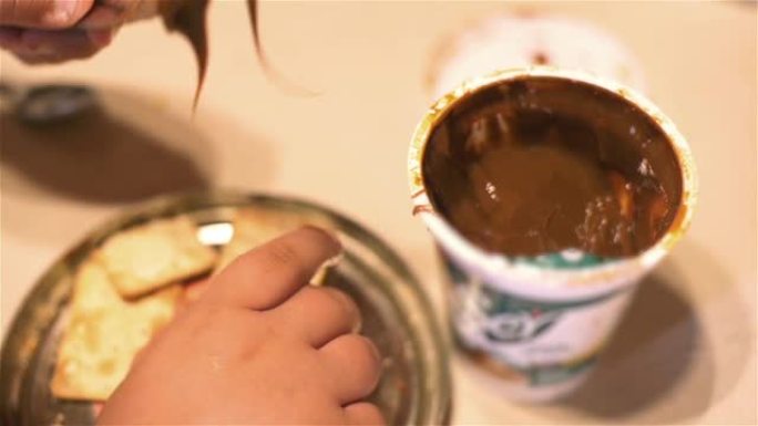 一个阿根廷小男孩的手吃早餐，把牛奶果酱撒在饼干上。特写。