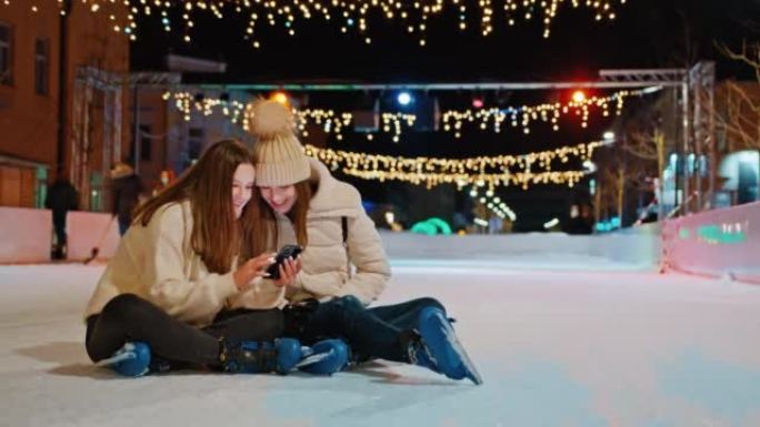 两名使用手机的年轻妇女坐在溜冰场上