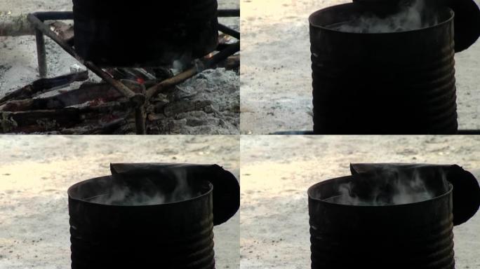 火上烹饪的食物，可折叠烤架上有水的金属锅在户外篝火上加热。特写。