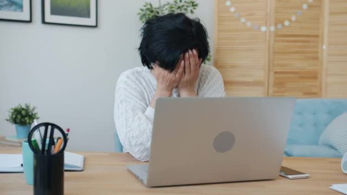 疲惫的女性自由职业者在家里用笔记本电脑打字，然后触摸面部感觉筋疲力尽