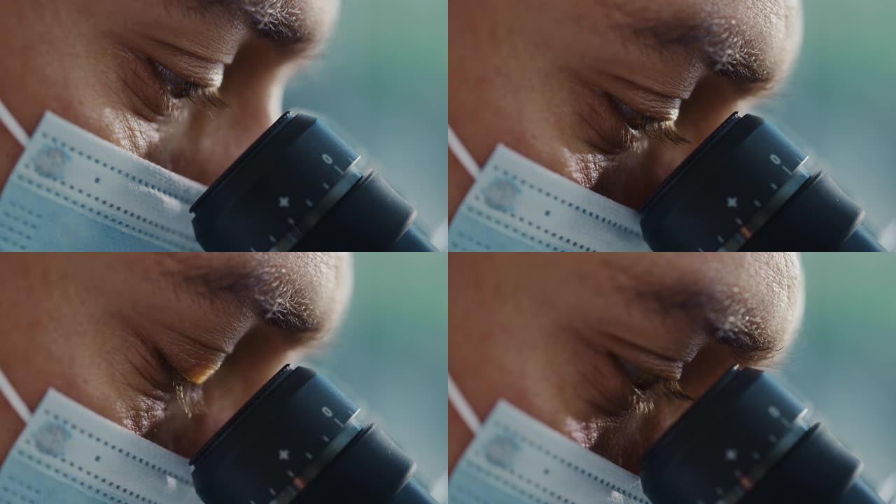 Ultra Macro特写了一名戴着外科口罩并看着显微镜的男性科学家的镜头。微生物学家使用技术设备在