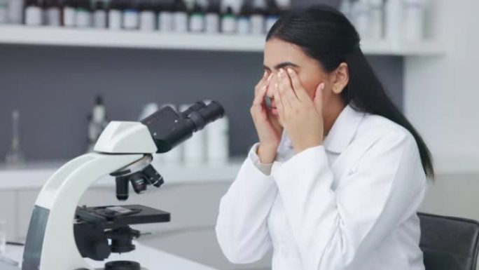 疲惫和疲惫的女人在实验室做研究时分析测试样本。压力很大的科学家通过显微镜观察，摩擦眼睛，在深夜工作时