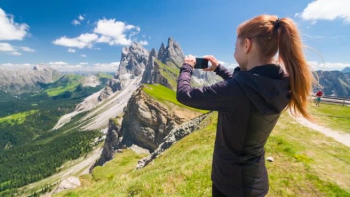女游客站在山顶上，在美丽的晴天用智能手机拍摄令人难以置信的景色