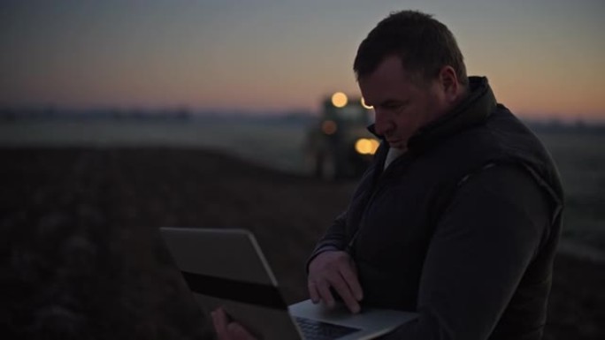 农民带着笔记本电脑在日出时在农田里工作