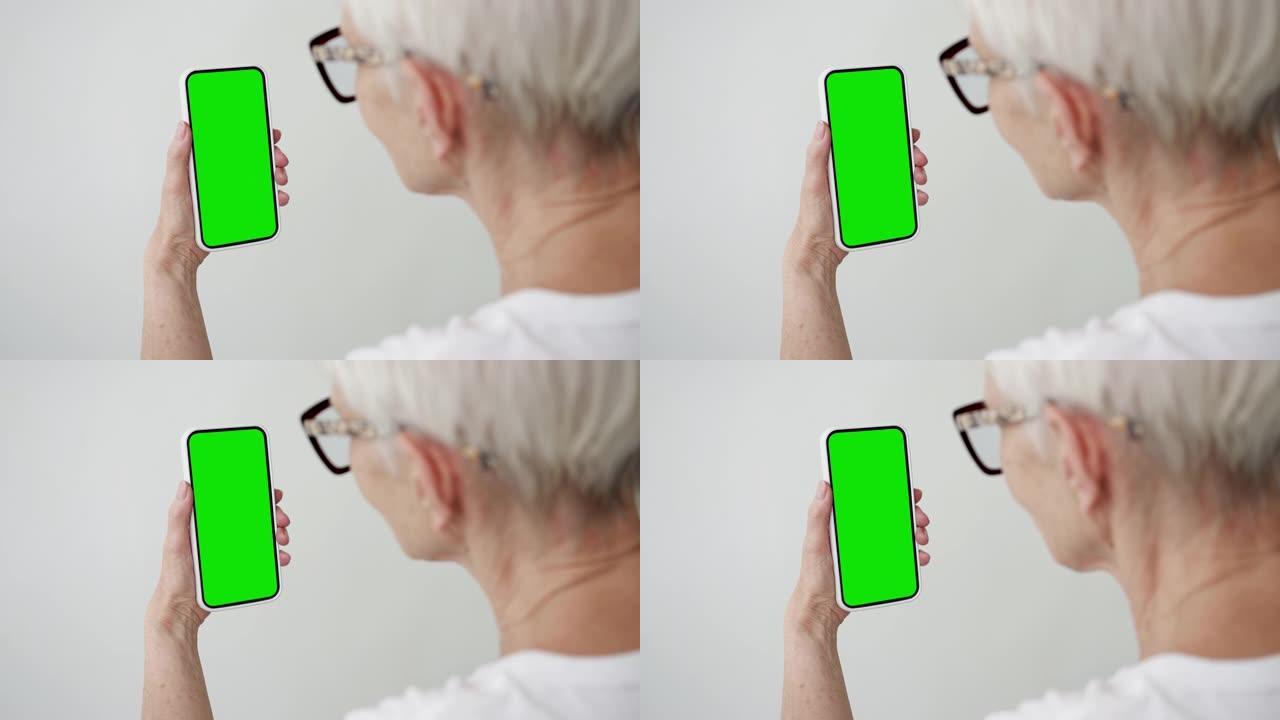 老妇人使用带有绿屏色度键特写的智能手机。老年人手持手机模型。概念观看和显示互联网社交媒体，视频通话，