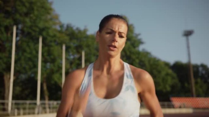 浅蓝色运动上衣美丽的女运动员在户外体育场跑得非常快。她在一个温暖的夏日下午冲刺。精女正在慢跑训练。肖