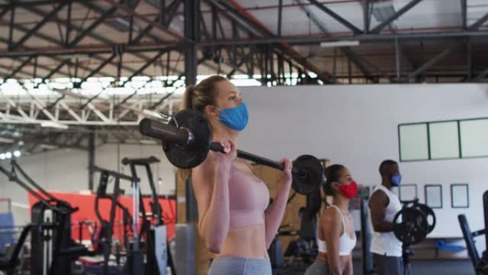 适合戴口罩的白人妇女在健身房用杠铃锻炼