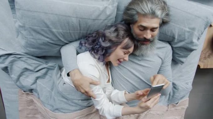 丈夫和妻子使用智能手机在床上欢笑和亲吻
