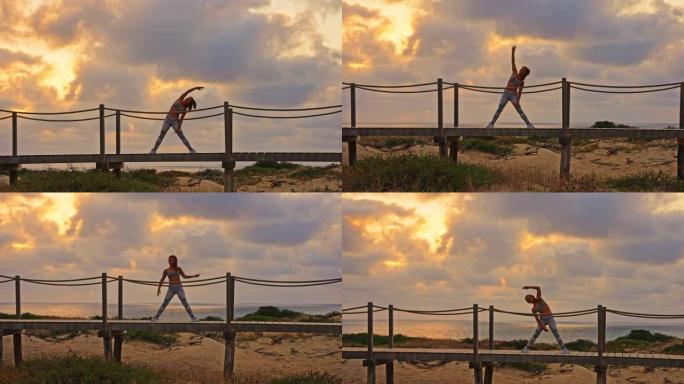 倾斜，在日落期间，无法辨认的健美女运动员在木板路上伸展的慢动作镜头