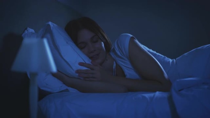 一名年轻的黑发女子正在关掉灯，在卧室舒适的床上，在温暖的羽绒被下安然入睡。舒适、放松、睡眠、健康、床