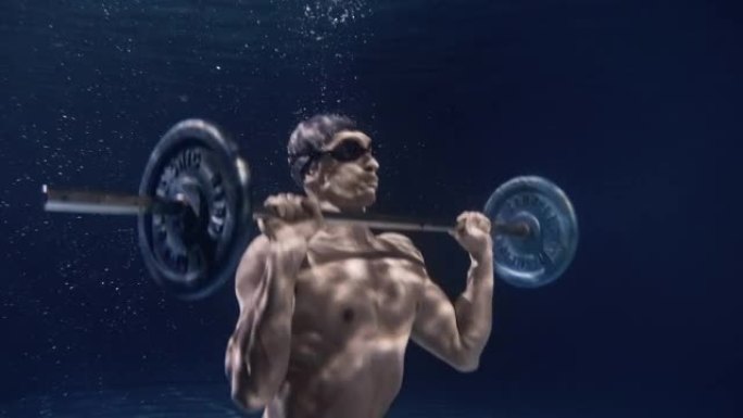 年轻的男性专业健美运动员的电影镜头，肌肉发达的身体正在水下用努力和决心举起杠铃。运动、健身、健康生活