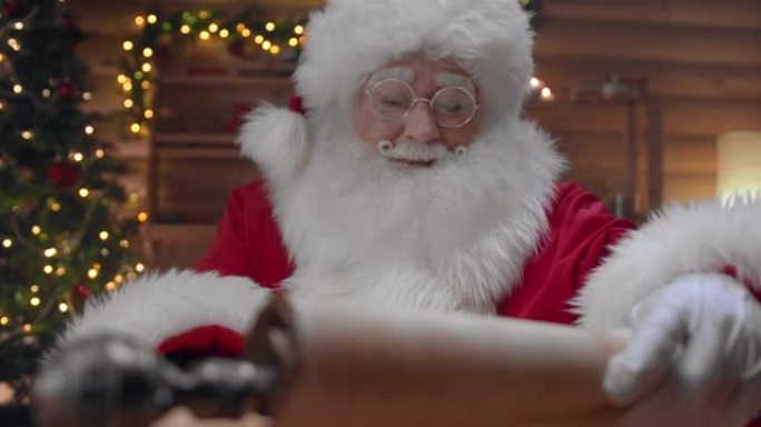 圣诞老人展开纸卷，坐在装饰精美的小屋中，圣诞树在他身后