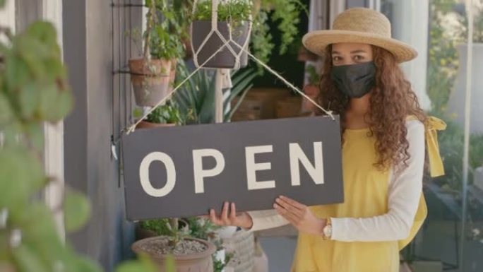 年轻的西班牙裔女花店戴着面具，早上在她的商店外面挂了一个开放标志